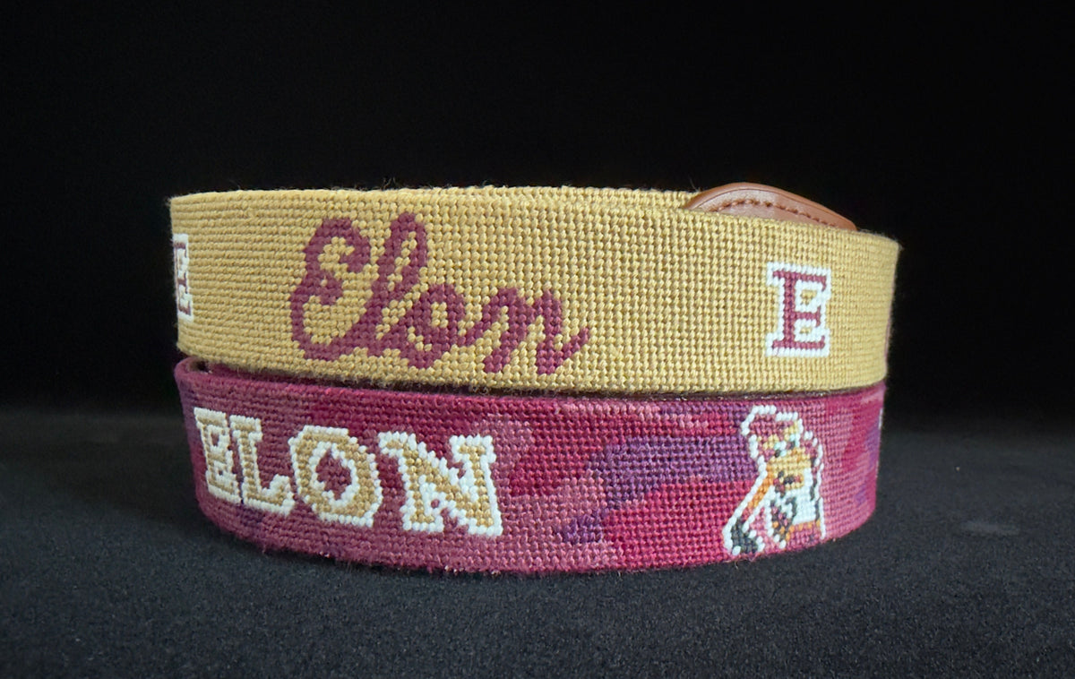 Two woven Elon brand belts stacked on a black background, one in gold with burgundy script and the other in burgundy with white block letters and a mascot graphic.